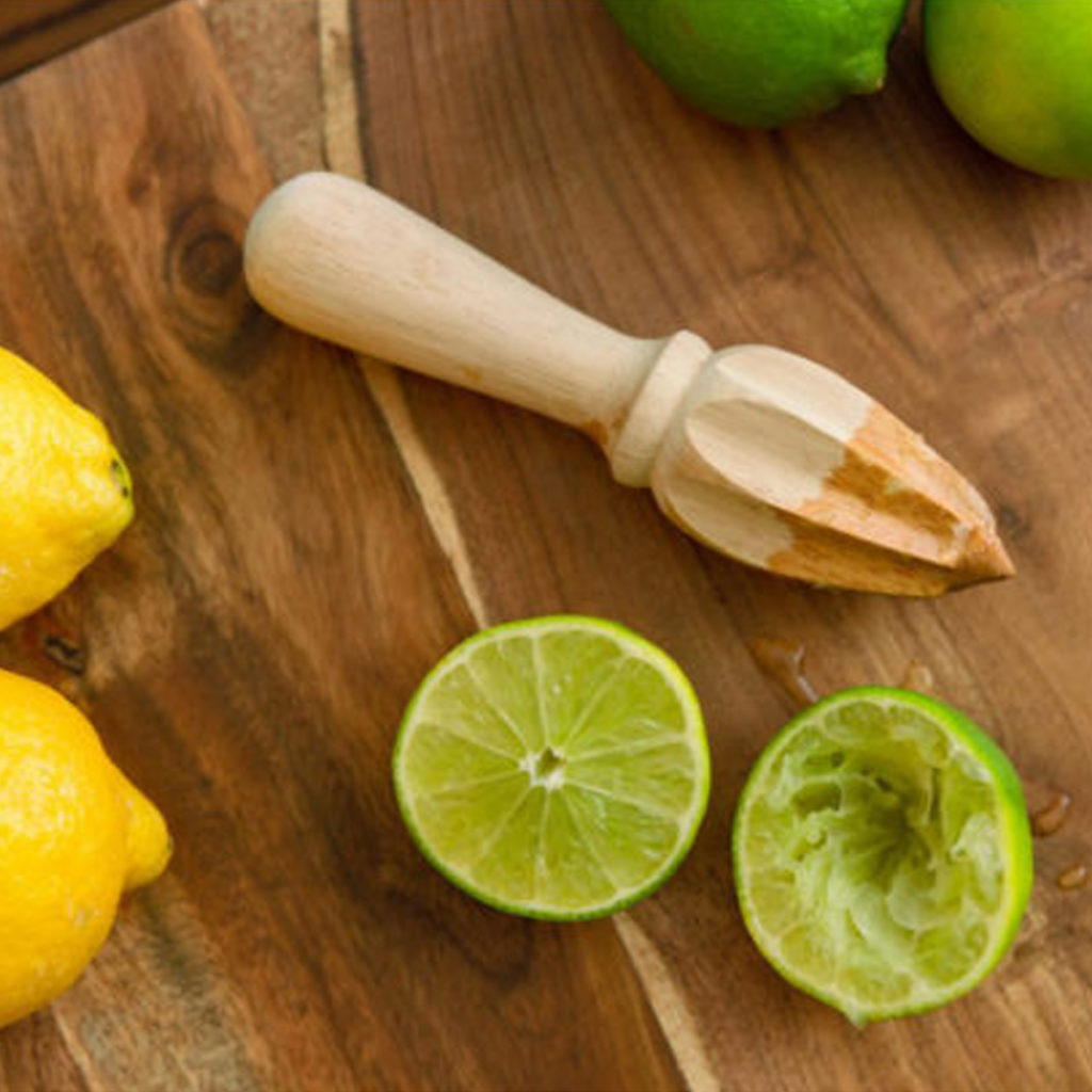 A wooden lemon reamer on a wooden table top surrounded by halved lemons and limes.