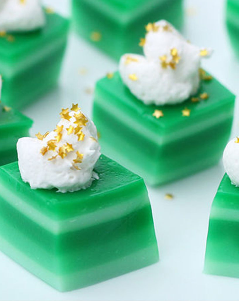 Green ombre jello shots with cream and glitter garnish.